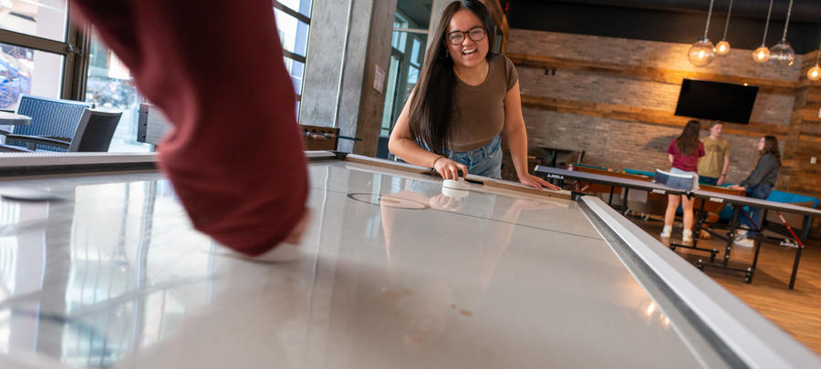 A University of Minnesota Rochester student smiles while playing air hockey with classmates.